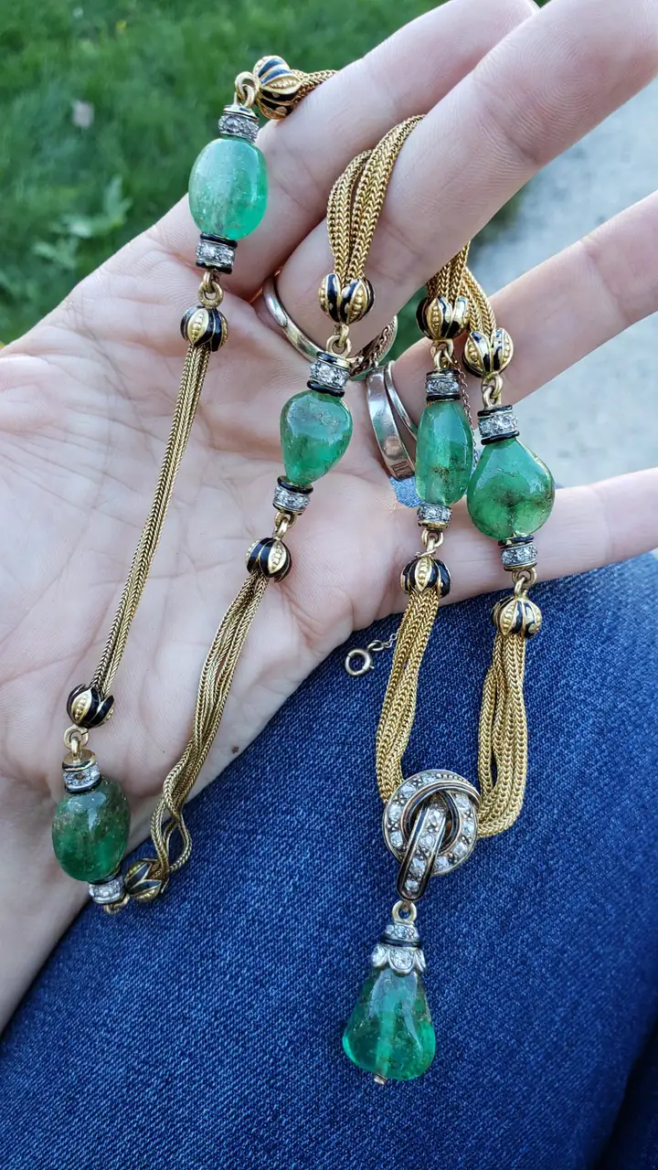 A gold necklace with green emerald beads and a drop pendant, held in the finder's hand.